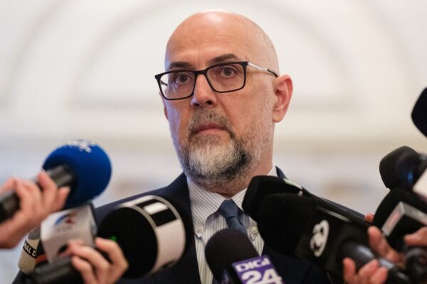 Bărbat chel cu ochelari răspunde presei la microfoane
