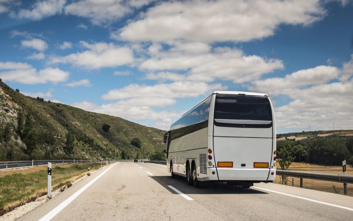 Autocar alb pe autostradă printre dealuri verzi