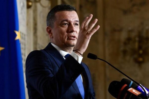 Bărbat la pupitru vorbind, steagul UE în fundal